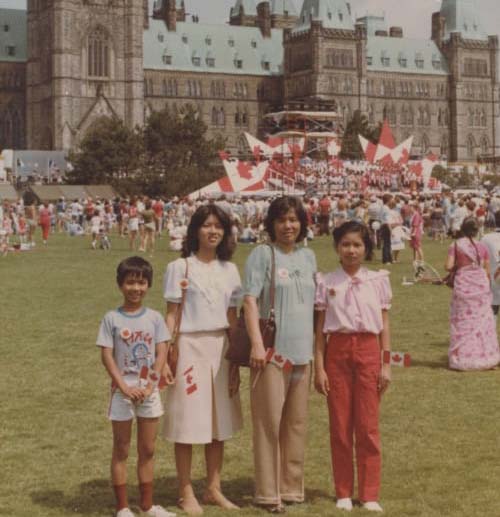 Quatre personnes avec des drapeaux du Canada devant le bâtiment du Parlement.